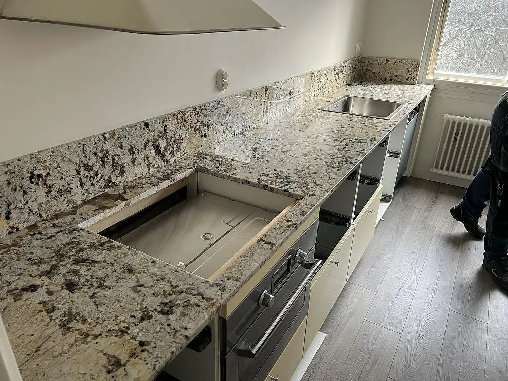 Poleret køkkenbordplade i Alaskan white granit i ett køkken i Enskede, monteret längs fönstervägg med synligt udskæring i stenen.