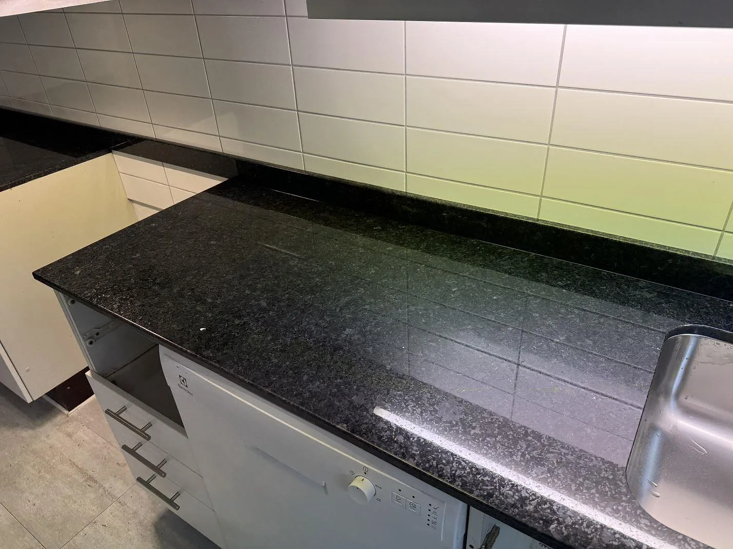 Køkkenbordplade i poleret granit Angola Black med låg stenkant og synlig rostfri vask i ett køkken i Malmö.