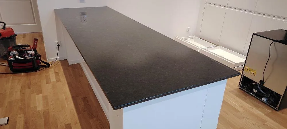 Køkkenbordplade i mørk Angola Black granit, poleret 20 mm, monteret på en hvid køkkenø under montering i Mjölby.