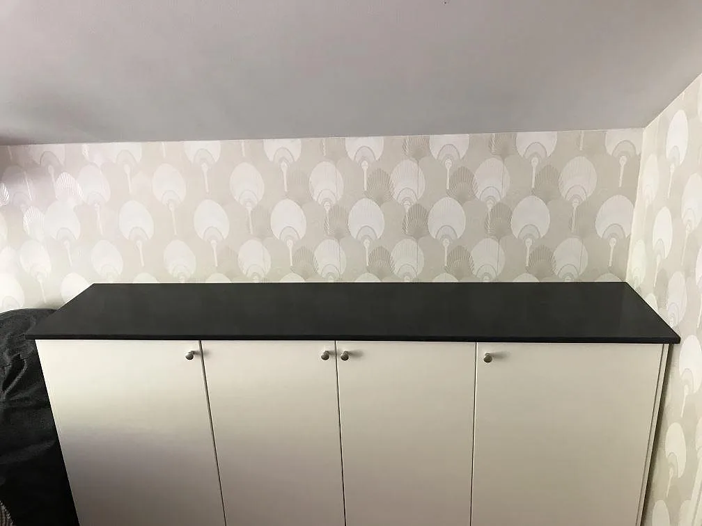 Bordplade i mørk antracitgrå Anthracite Elegante, poleret kvartskomposit, monteret på vita skabe mot mönstrad tapet i Helsingborg.