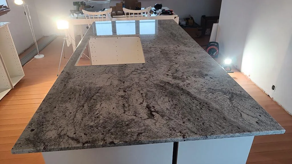 Køkkenø i Antique White granit, poleret, med öppen urtagning og tydlig svartgrå åretegning i ett køkken under montering i Båstad.