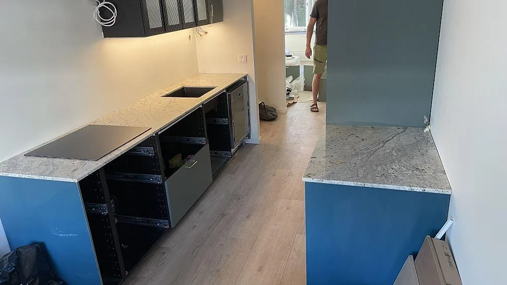 Køkkenbordplade i poleret Antique White granit med kogeplade og vask i ett køkken under montering i Helsingborg.