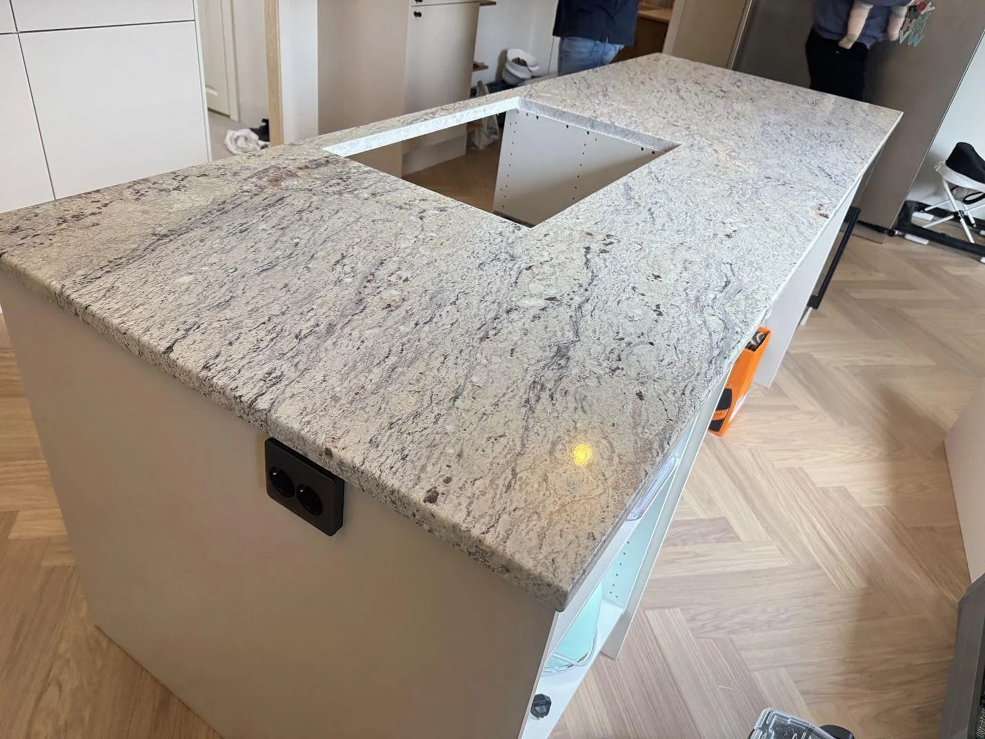Køkkenø med poleret Bordplade i graniten Antique White og öppning for kogeplade i ett køkken under montering i Lund.