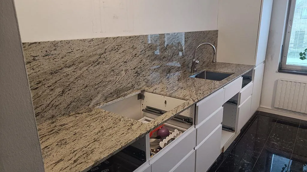 Køkkenbordplade i Antique White granit, poleret 20 mm, med stænkplade og rostfri vask i ett køkken i Malmö under montering.