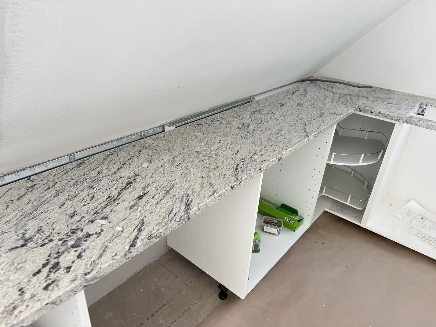 L-formad køkkenbordplade i Antique White granit, poleret, på vita köksstommar under montering i Simrishamn.