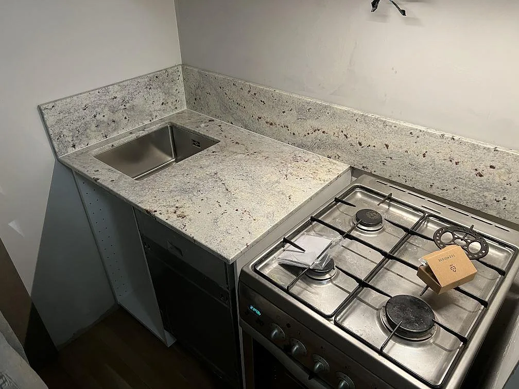 Køkkenbordplade i poleret Antique White granit med stänkkant og fristående komfur i ett køkken i Solna.