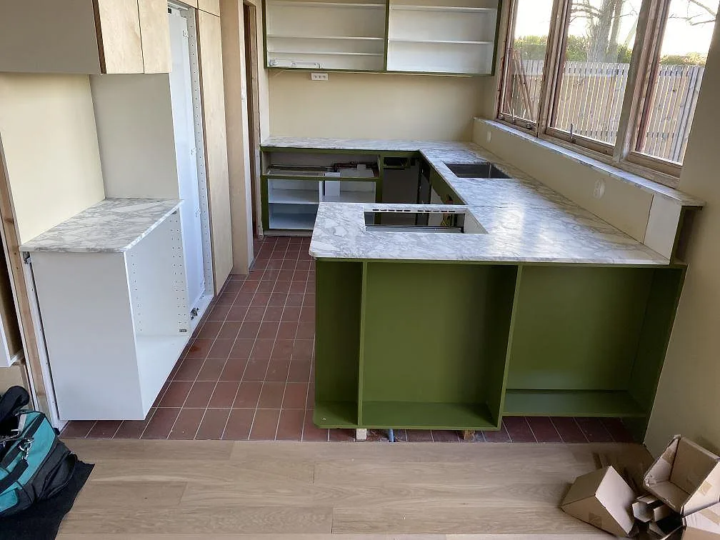Køkkenbordplade i mat Arabescato-marmor med halvö, hällöppning og uppvikta stänkkanter i ett køkken under montering i Limhamn.