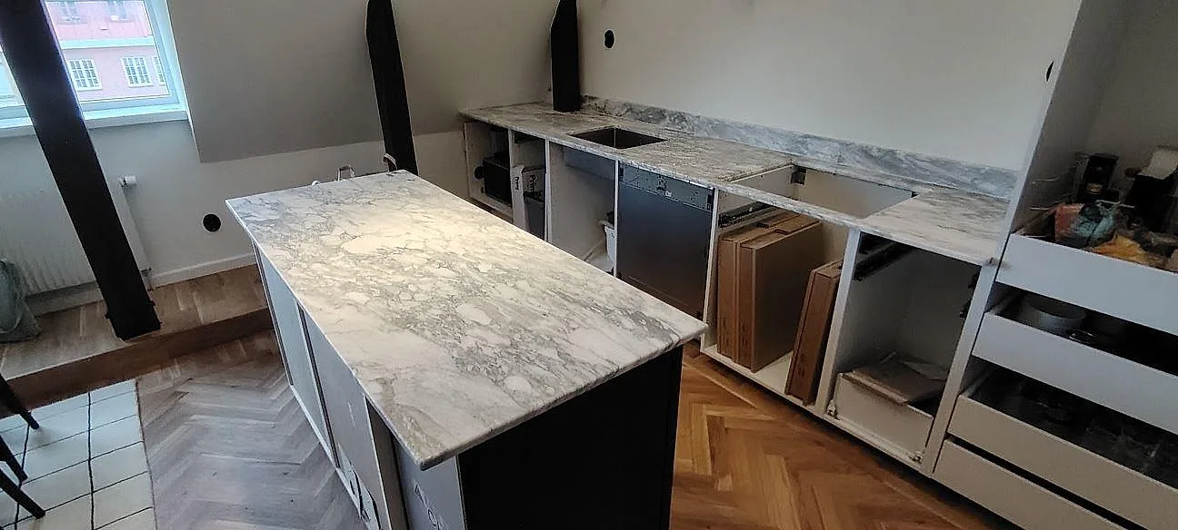Køkkenbordplade og køkkenø i hvid Arabescato marmor, mat, med grå teckning på öppna köksstommar under montering i Stockholm.