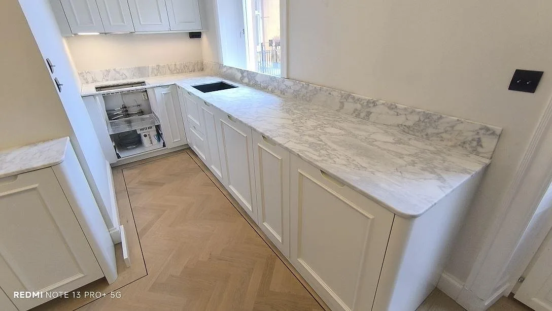 Køkkenbordplade i hvid Arabescato marmor, mat, med grå åretegning og uppvikt stænkplade i ett køkken i Stockholm.