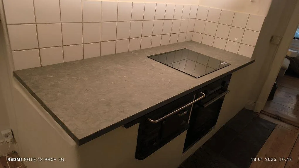 Køkkenbordplade i grå Azul Valverde marmor, mat, med kogeplade og kaklad væg i ett køkken i Stockholm.
