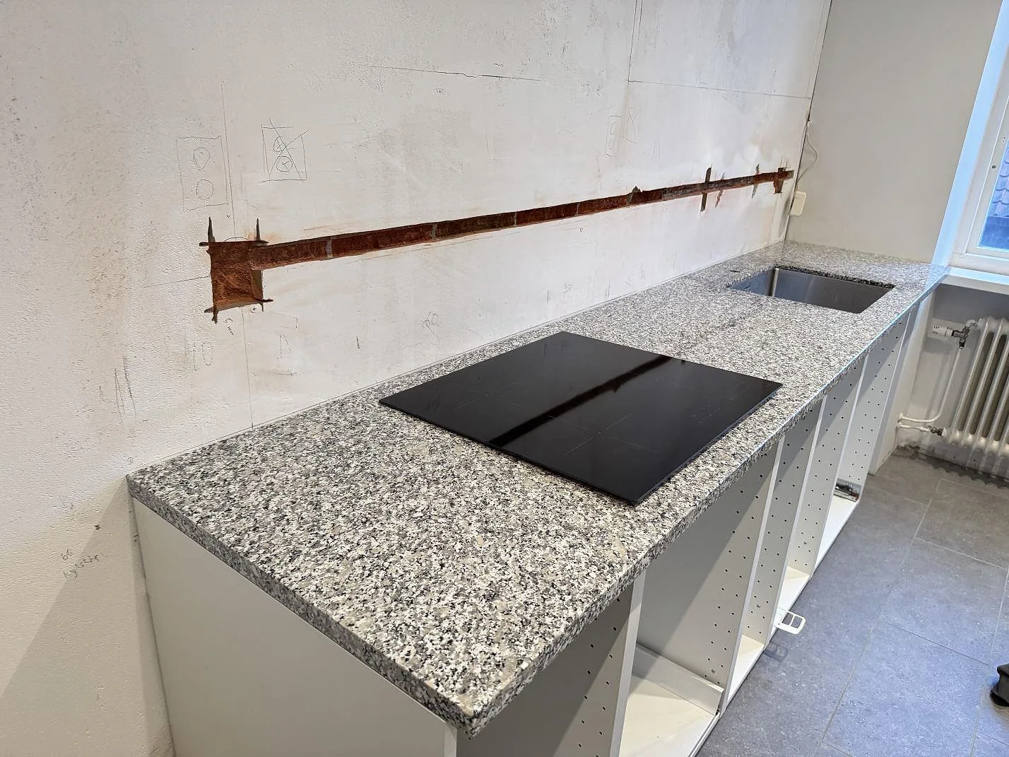 Køkkenbordplade i poleret Bianco Sardo granit med sort kogeplade og rostfri vask under montering i Helsingborg.