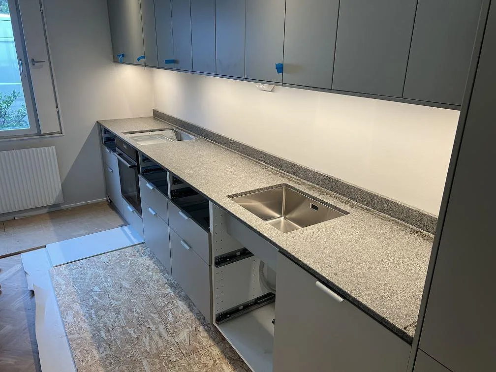 Mat køkkenbordplade i Bohus Grå granit med underlimmad rostfri vask, hällurtag og låg stänkkant i ett køkken i Lidingö.
