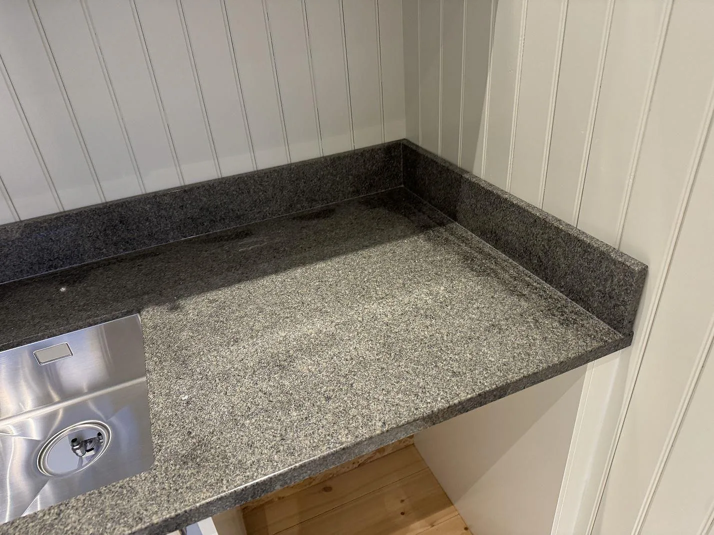 Køkkenbordplade i Bohus Grå granit, poleret, med låg stänkkant og rostfri vask i ett køkken under montering i Säffle.