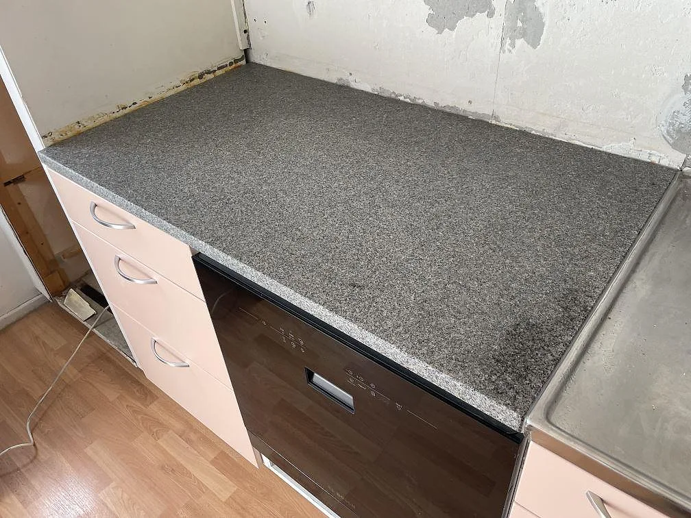Mat køkkenbordplade i Bohus Grå granit, 30 mm, monteret over lyse lådor i ett køkken i Solna under montering.
