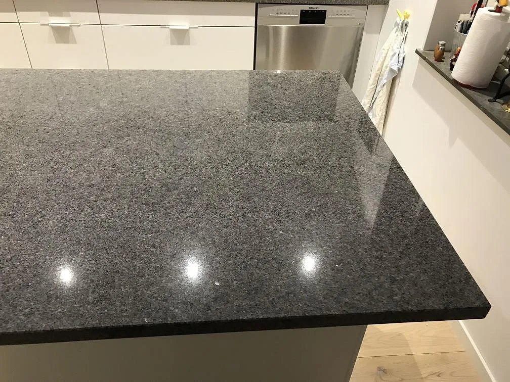 Køkkenbordplade og køkkenø i grå Bohus Grå-granit, poleret, i ett køkken i Växjö med vita skabe og infällda spotlights.