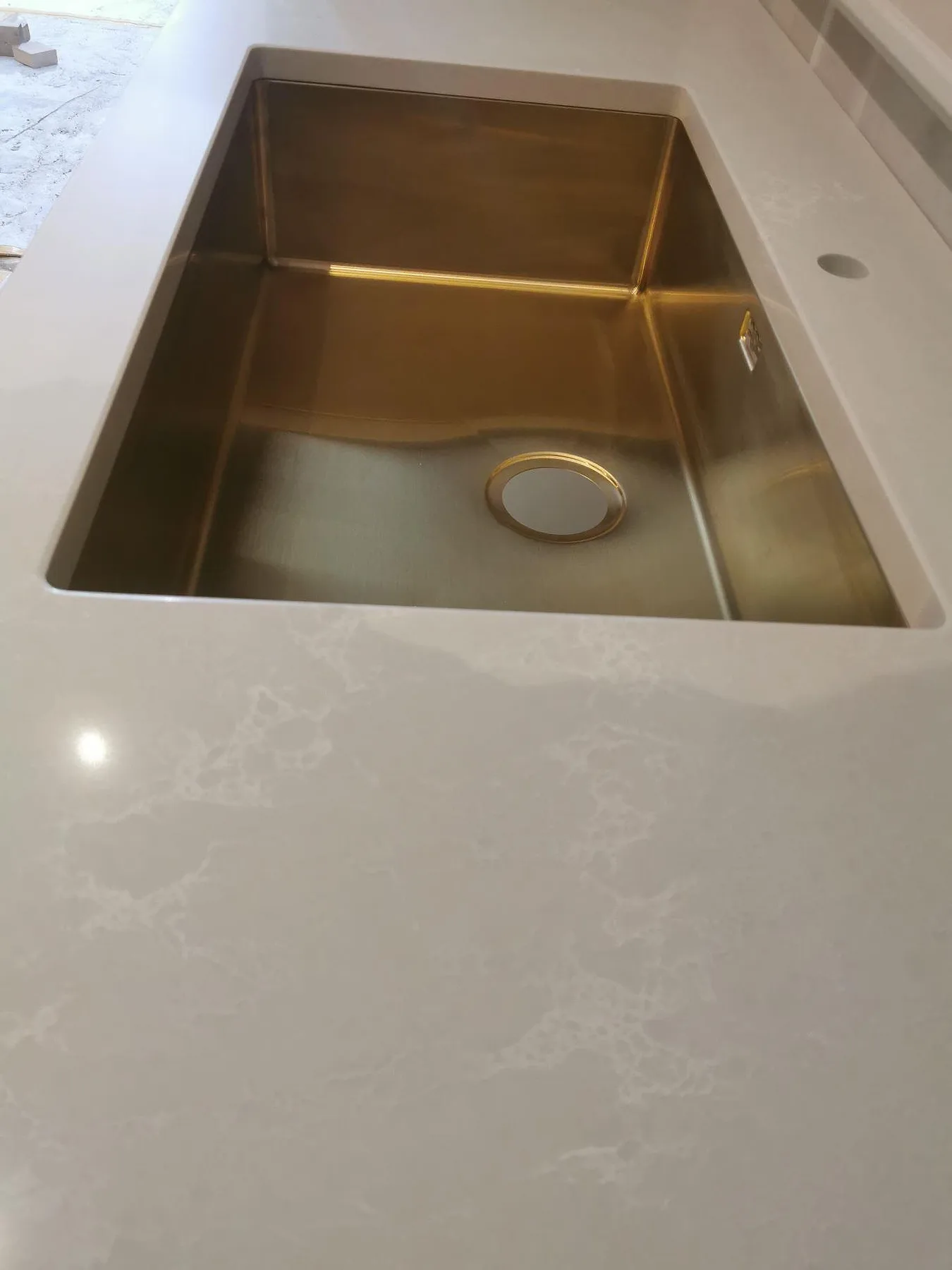 Køkkenbordplade i hvid Caesarstone Alpine Mist, poleret kvartskomposit med blød grå åretegning, med underlimmad vask i mässingston og borrat Armaturhul i ett køkken i Ekerö.