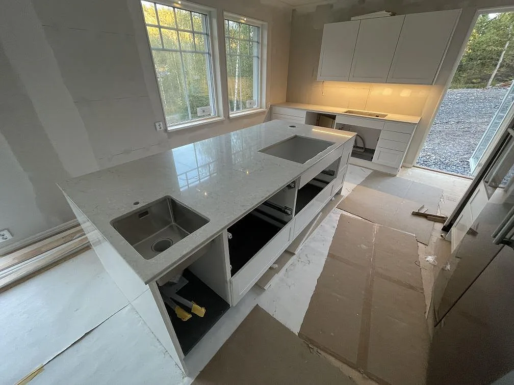 Køkkenbordplader i Caesarstone Bianco Drift, poleret hvid kvartskomposit, med køkkenø, underlimmad vask og väggbänk i Åkersberga.