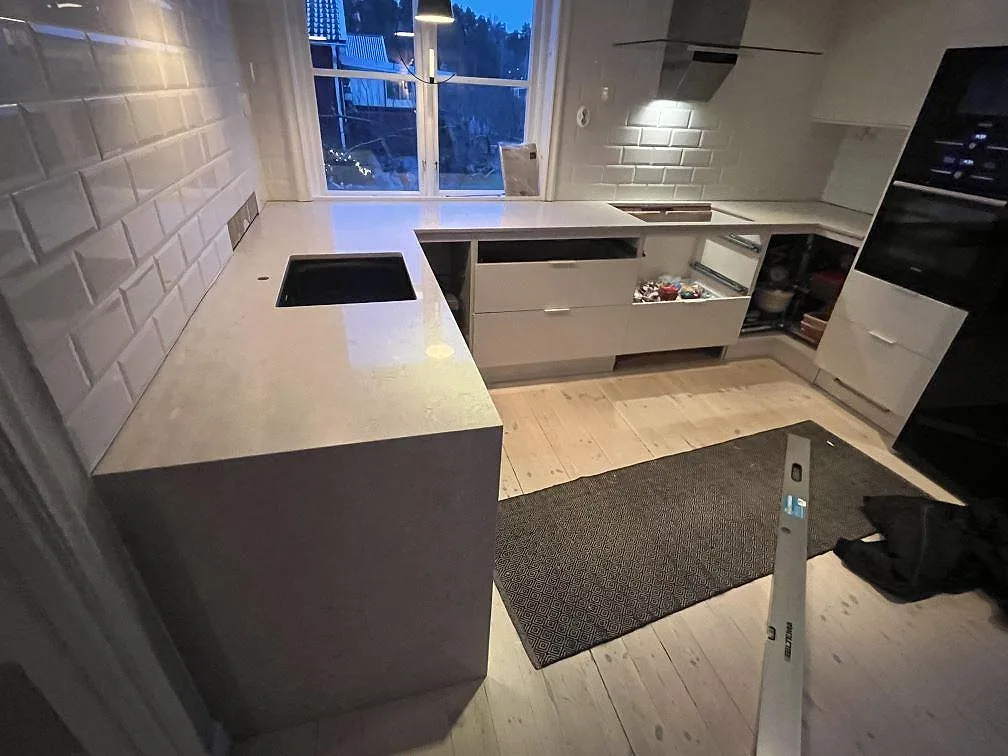 Køkkenbordplade i lys Caesarstone Bianco Drift, poleret komposit, med køkkenø, perimeterbänkar og hällzon i ett køkken i Bromma.