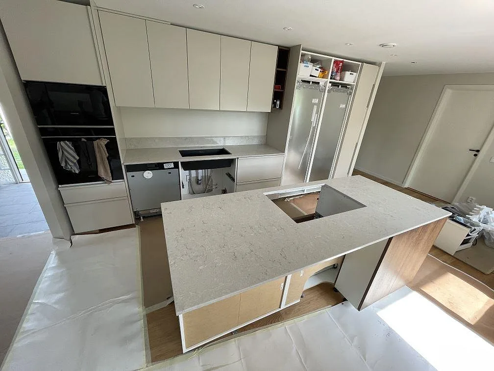 Køkkenbordplade og køkkenø i Caesarstone Bianco Drift, poleret hvid kvartskomposit med grå åretegning, under montering i ett køkken i Ekerö.