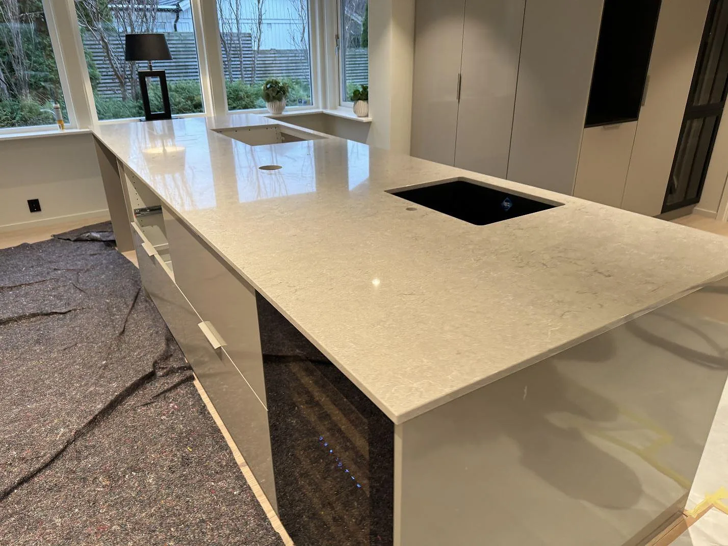 Køkkenbordplade i poleret Caesarstone Bianco Drift kvartskomposit med sort underlimmad vask og hällöppning i ett køkken i Halmstad.