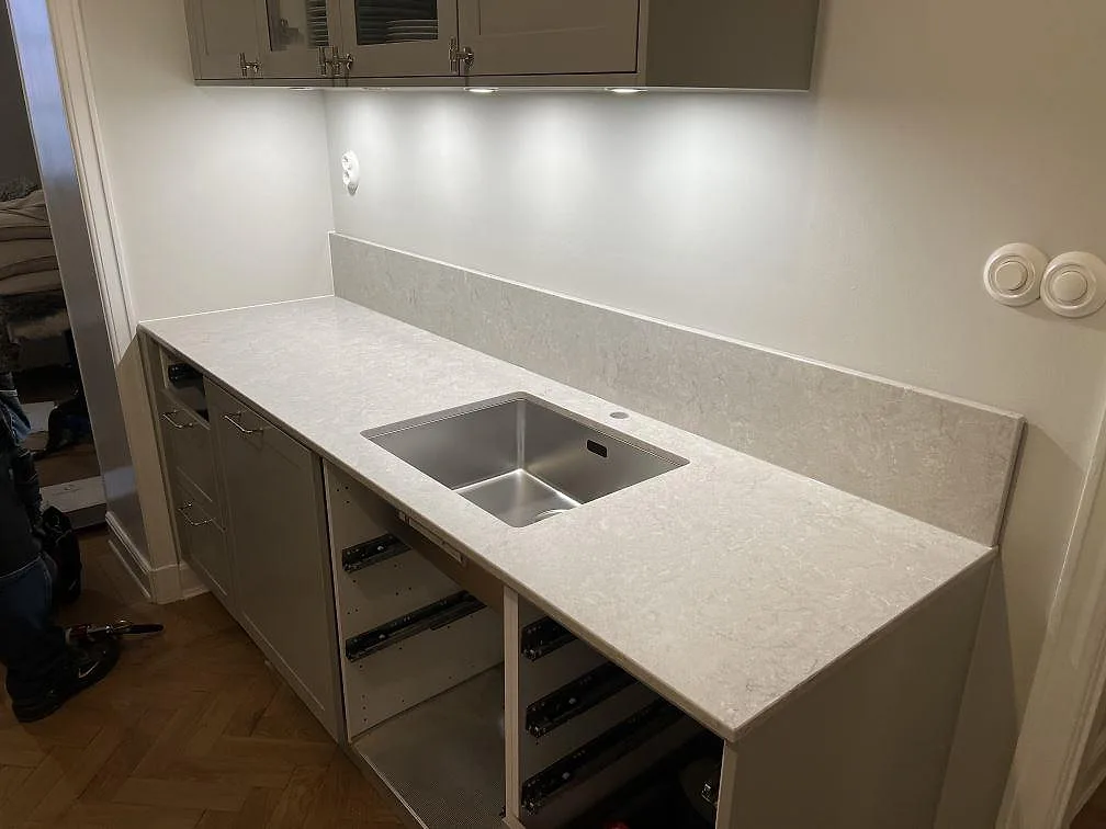 Køkkenbordplade i Caesarstone Bianco Drift, poleret komposit, med uppvikt stänkkant og rostfri vask i ett køkken i Stockholm.