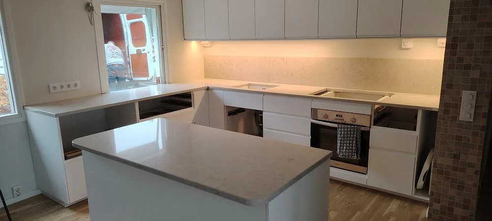 Poleret køkkenbordplade i Caesarstone Bianco Drift, hvid kvartskomposit med blød grå åretegning, på køkkenø og bänkrad i ett køkken i Täby.