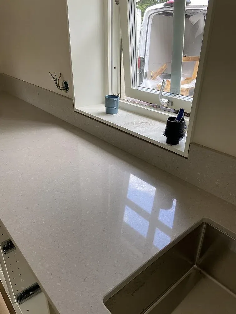 Køkkenbordplade i Caesarstone Clamshell, poleret beige kvartskomposit, med underlimmad rostfri vask vid fönstret i ett køkken i Emmaboda.