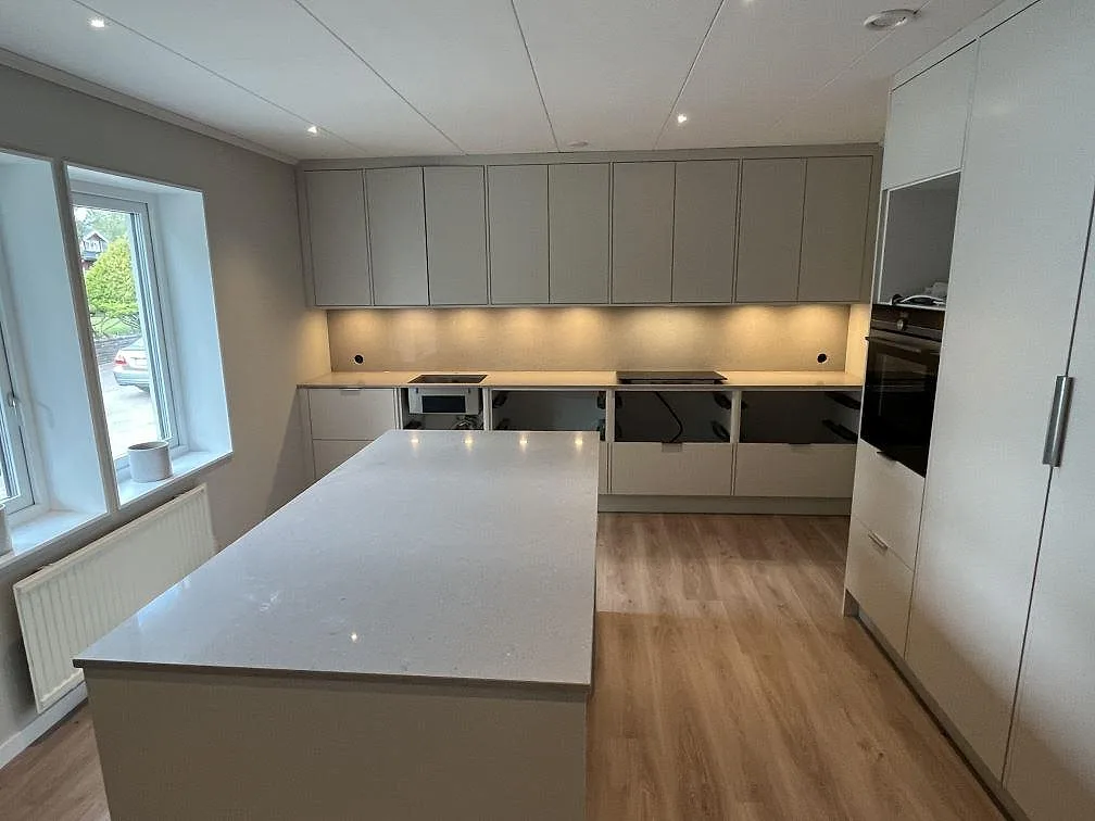 Køkkenbordplade og køkkenø i beige Caesarstone Clamshell komposit, poleret, i ett ljust køkken under montering i Halmstad.