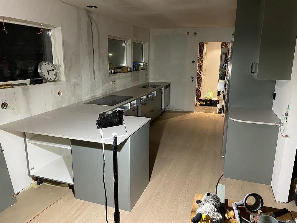 Køkkenbordplade i mat Caesarstone Clamshell, ljusgrå kvartskomposit, med køkkenø og väggbänk i ett køkken under montering i Lerum.