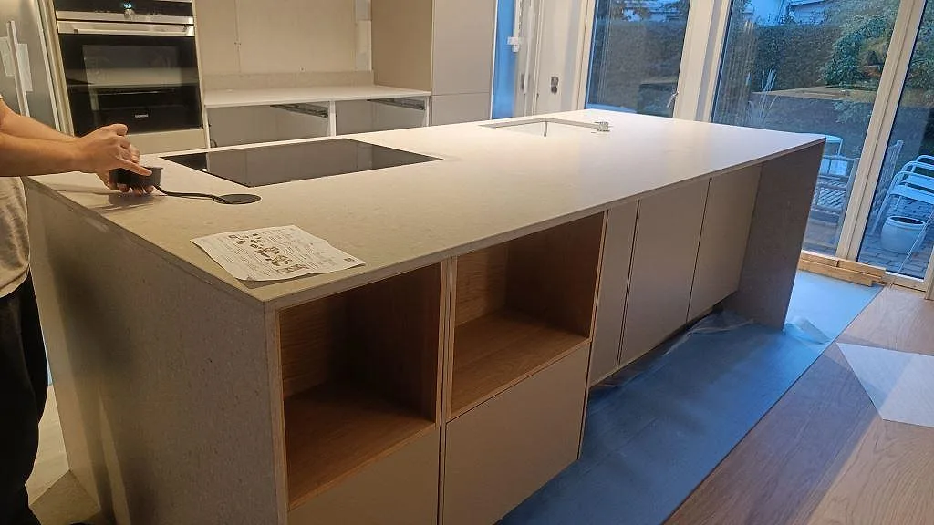 Køkkenbordplade og køkkenø i Caesarstone Clamshell, mat beige kvartskomposit, med nedsänkt induktionshäll i ett køkken i Lomma.