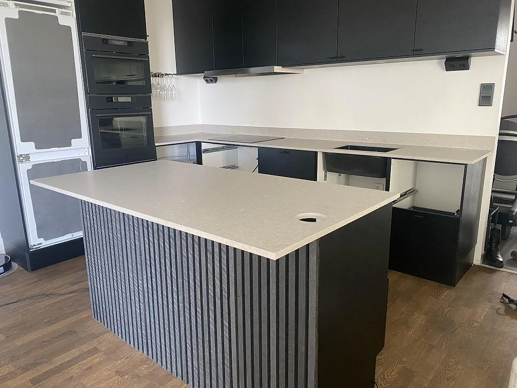Køkkenbordplade i krämvit Caesarstone Clamshell, mat kvartskomposit, i ett U-format køkken med køkkenø og mørke skabe i Malmö.