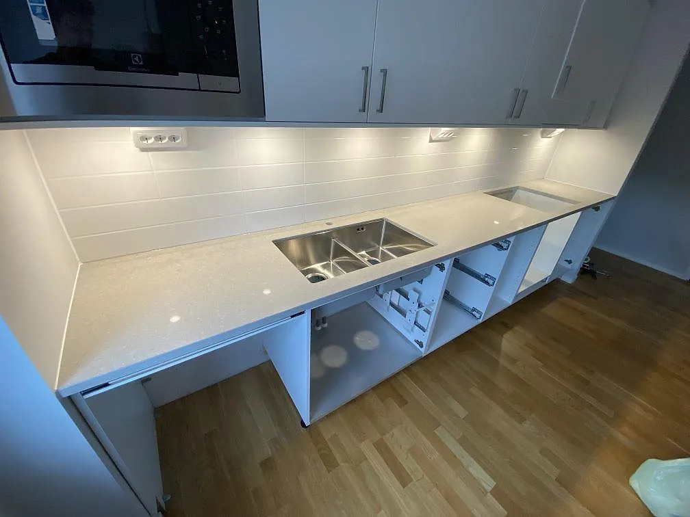 Køkkenbordplade i poleret Caesarstone Clamshell, lys kvartskomposit, med underlimmad rostfri dubbelho og hällurtag i ett køkken i Malmö.