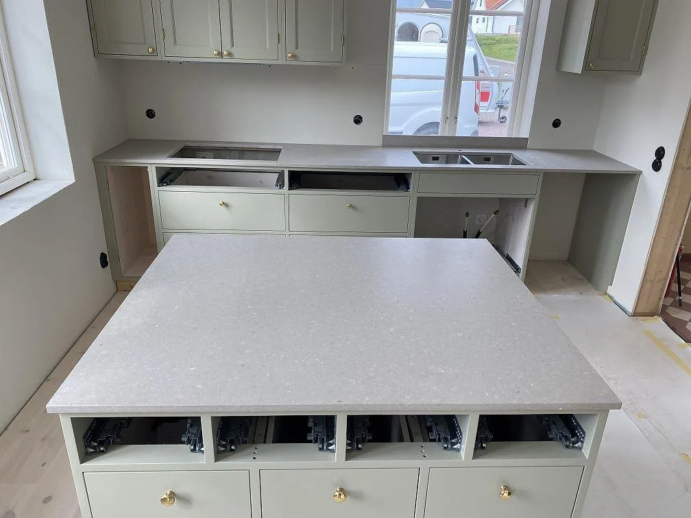 Køkkenbordplade i mat Caesarstone Clamshell komposit med stor køkkenø og bakre arbetsbänk i ett køkken i Stehag.