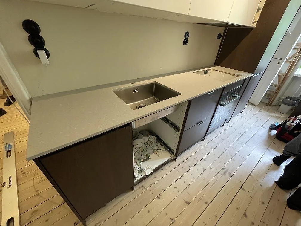Køkkenbordplade i mat Caesarstone Clamshell, lys beige kvartskomposit, med underlimmad vask og hälluttag i ett køkken i Stockholm.