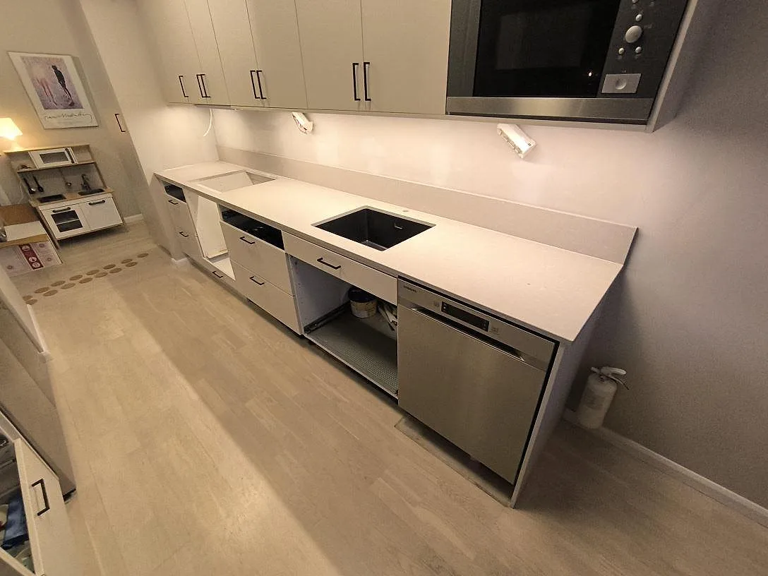 Køkkenbordplade i Caesarstone Clamshell, poleret kvartskomposit, med sort vask, hälluttag og låg stänkkant i ett køkken i Stockholm.