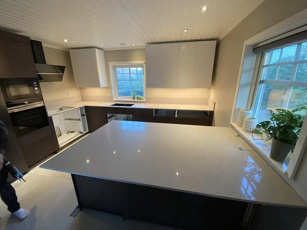 Køkkenbordplade og stor køkkenø i krämig Caesarstone Clamshell, poleret kvartskomposit, i ett køkken under montering i Torslanda.