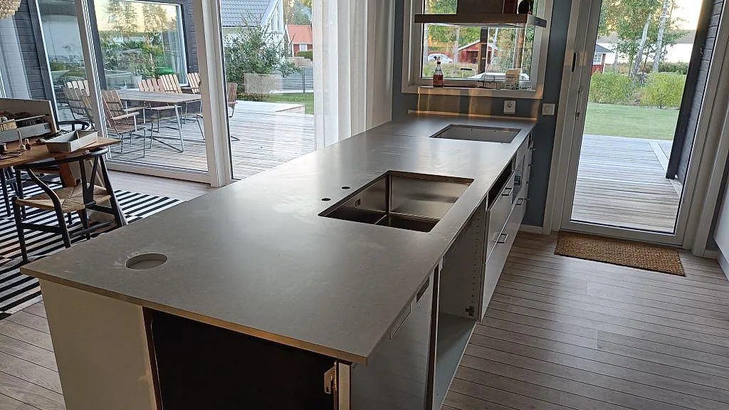 Køkkenbordplade i mat Caesarstone Clamshell, grå kvartskomposit, med underlimmad rostfri vask og hällöppning i ett køkken på Torsö.