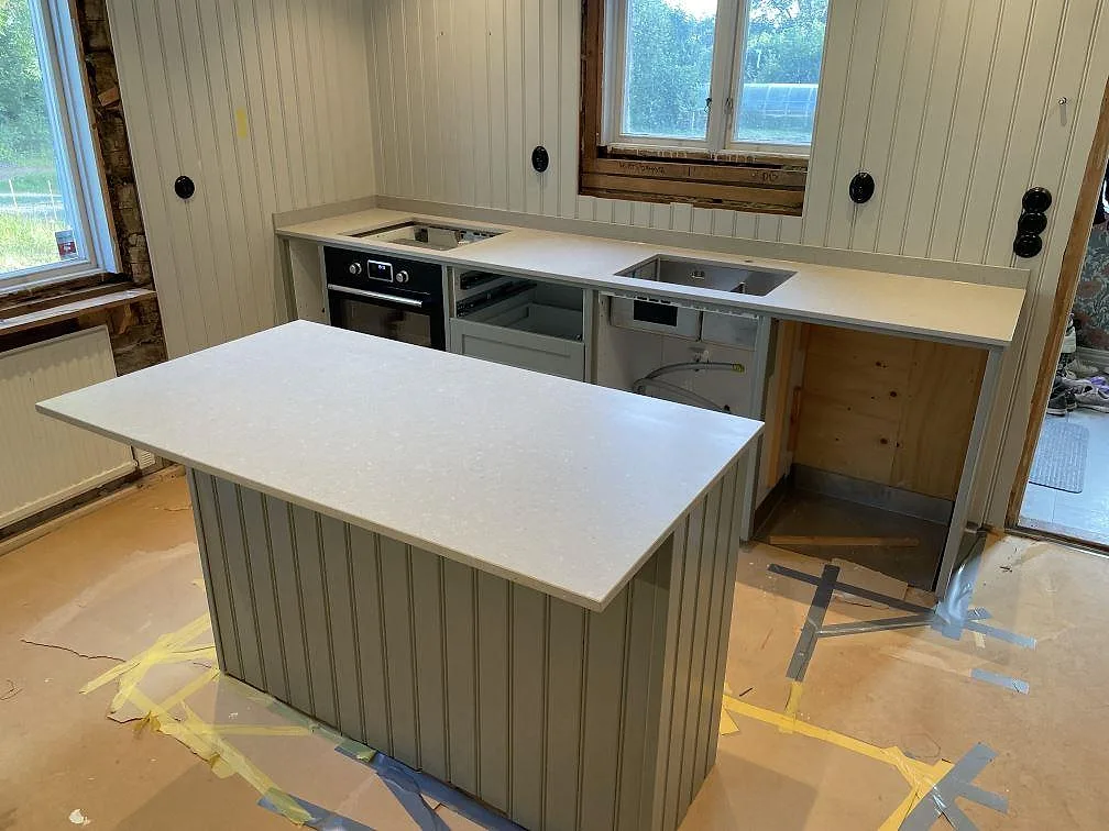 Køkkenø og køkkenbordplade i mat Caesarstone Clamshell kvartskomposit, med synlig vask og hällöppning under montering i Uppsala.