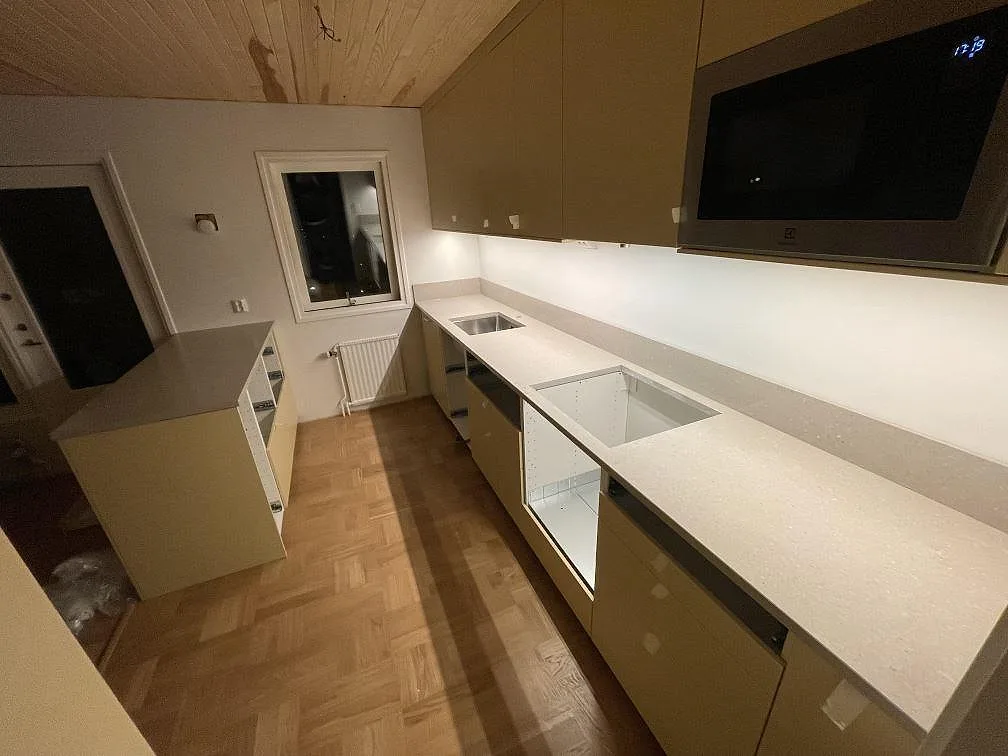 Poleret køkkenbordplade i Caesarstone Clamshell, lys kvartskomposit, med låg stänkkant og udskæring i ett køkken i Vällingby.