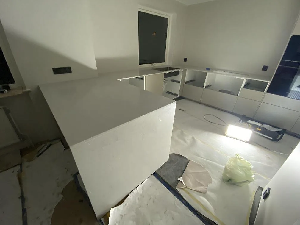 Poleret køkkenbordplade i Caesarstone London Grey, 20 mm komposit, med bred halvö og öppna köksstommar under montering i Lund.