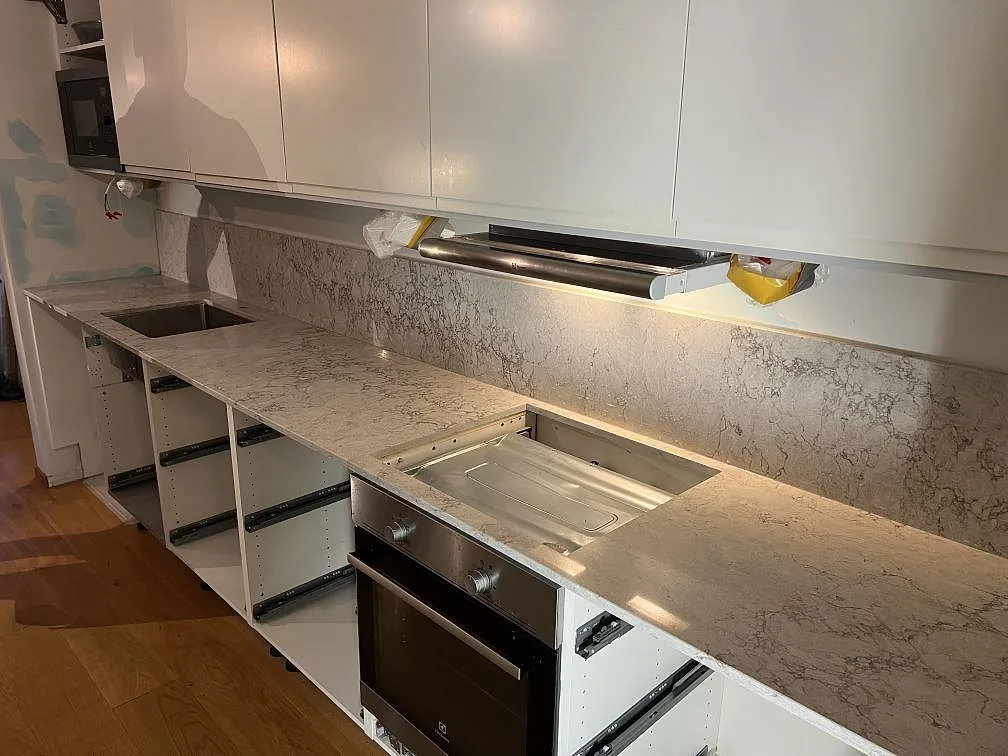 Køkkenbordplade i Caesarstone Moorland Fuge, 20 mm poleret kvartskomposit, med matchande stænkplade og kogeplade under montering i Bromma.