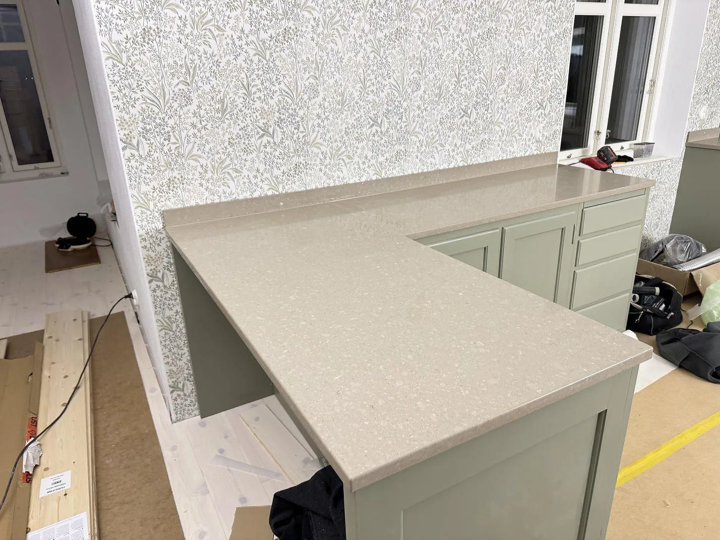 Køkkenbordplade i Caesarstone Shitake, poleret gråbeige kvartskomposit, med L-formad arbetsyta og uppvikt stänkkant i ett køkken i Hörby.