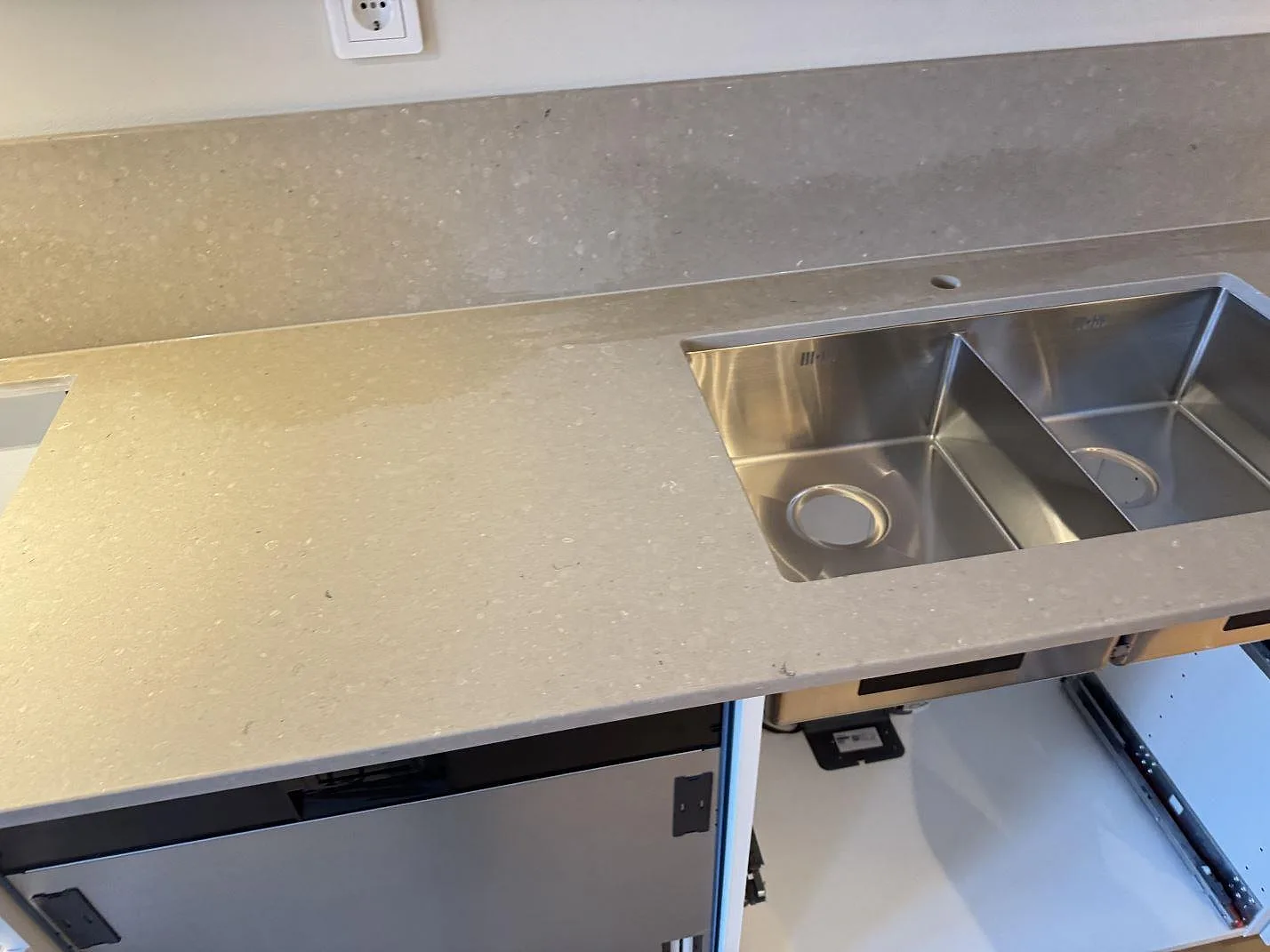 Køkkenbordplade i Caesarstone Shitake, varm gråbeige kvartskomposit med mat overflade, med underlimmad dubbelho i Rustfrit stål og uppvikt stænkplade i ett køkken i Malmö.