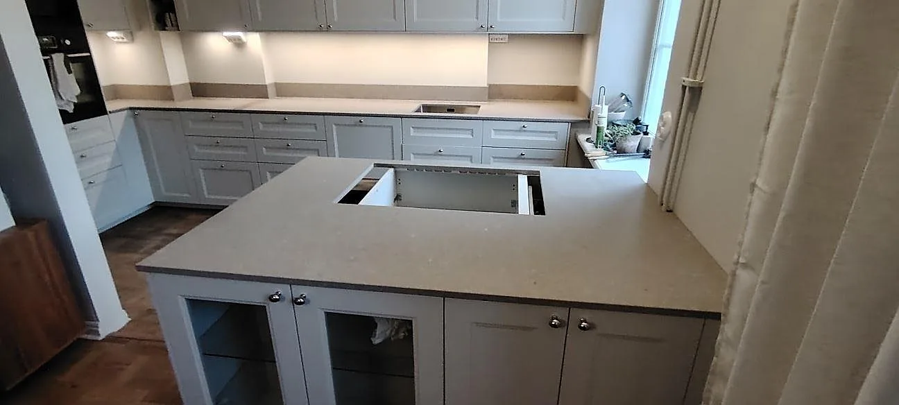 Køkkenø i Caesarstone Shitake, mat beige kvartskomposit, med hällöppning foran lyse Bordplader og stänkkant i ett køkken under montering i Stockholm.