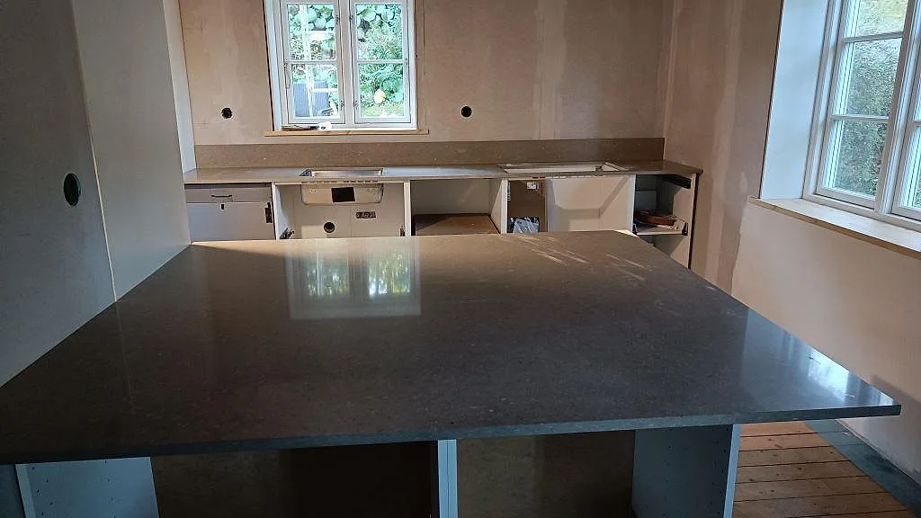 Køkkenbordplade og stor køkkenø i Caesarstone Shitake, poleret taupegrå kvartskomposit, under montering i ett køkken i Västra Frölunda.