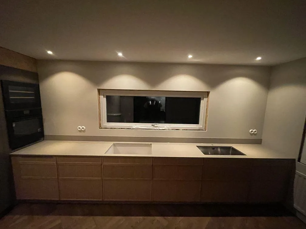 Køkkenbordplade i Caesarstone Shitake, mat brungrå kvartskomposit, längs en väggbänk med hällurtagning og underlimmad rostfri vask i ett køkken i Varberg.