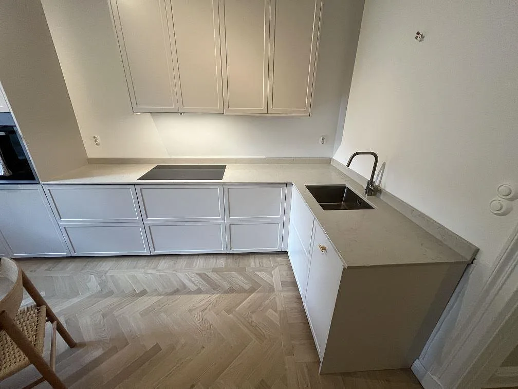 Køkkenbordplade i lys Caesarstone Taj Royale, poleret komposit, med synlig vask og kogeplade i ett L-format køkken i Stockholm.