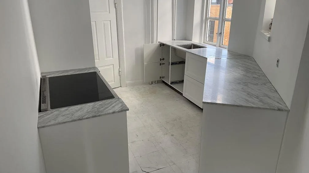 Køkkenbordplade i Carrara C marmor, mat 20 mm, i ett smalt vitt køkken med komfur og vask i Aarhus C.