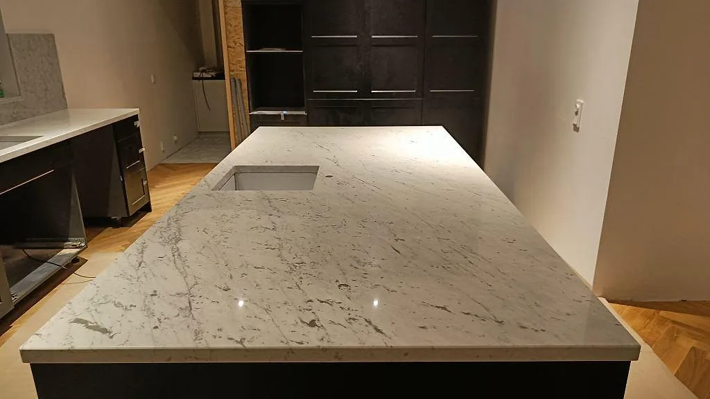Køkkenbordplade og køkkenø i hvid Carrara C marmor med grå åretegning, poleret, med underlimmad rostfri vask i ett køkken i Bara.