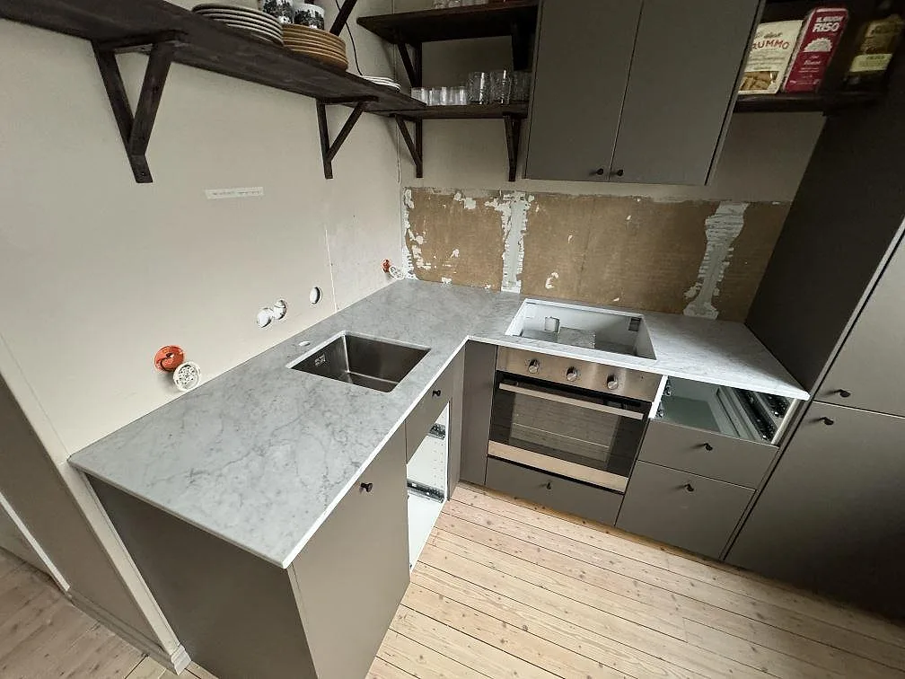 L-format køkken i Borås med mat Carrara C marmorbordplade, rostfri vask og udskæring for kogeplade under pågående montering.